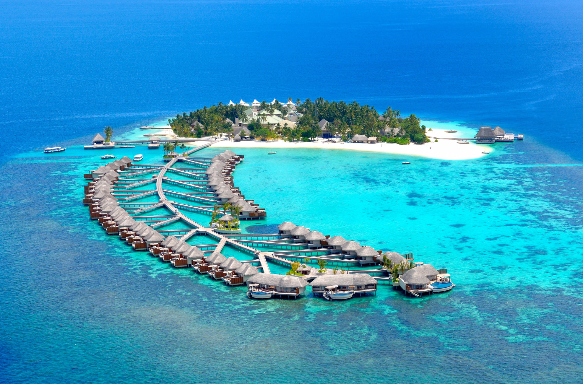 Aerial view of a Maldives resort with overwater villas curving into a turquoise lagoon